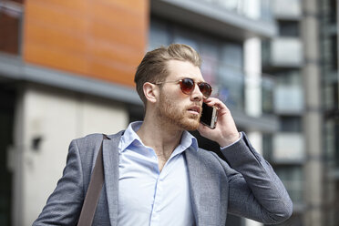 Junger Geschäftsmann mit Sonnenbrille, der vor seinem Büro mit seinem Smartphone spricht, London, Großbritannien - CUF21007