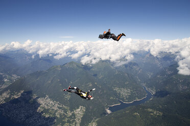 Freestyle skydiving team training together. One man performing air-ballet, another jumper is filming with video camera on helmet, Locarno, Tessin, Switzerland - CUF21010