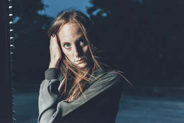 Portrait of young freckled woman with hand in long red hair at night - CUF21122