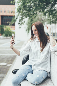 Junge Frau sitzt an der Wand und macht ein Selfie mit ihrem Smartphone - CUF21128
