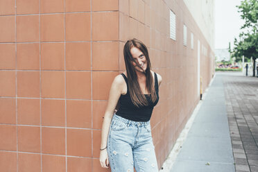 Portrait of young woman with red hair leaning against corner wall - CUF21137