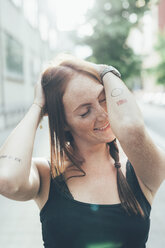 Junge Frau mit langen roten Haaren und Sommersprossen mit geschlossenen Augen auf der Straße - CUF21140