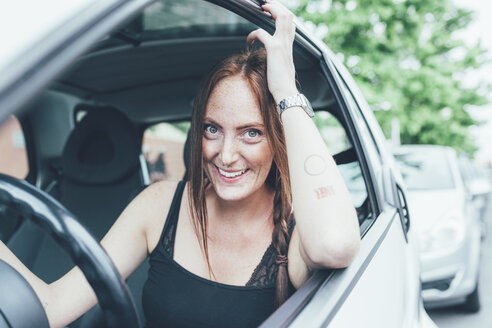 Porträt einer jungen Frau mit langen roten Haaren und Sommersprossen am Autofenster - CUF21141