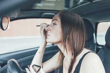 Young woman with freckles applying eyeshadow in car mirror - CUF21142