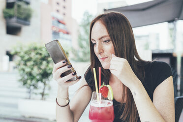 Young woman at sidewalk cafe reading smartphone texts - CUF21143