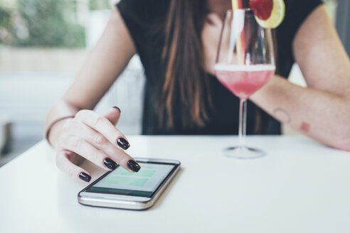 Ausgeschnittene Aufnahme einer jungen Frau am Tisch eines Straßencafés, die den Touchscreen ihres Smartphones benutzt - CUF21144