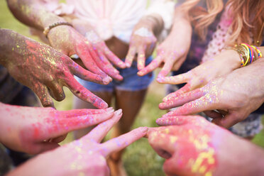 Group of friends at festival, covered in colourful powder paint, connecting fingers with peace signs, close-up - CUF21192