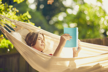 Teenage boy relaxing in garden hammock reading a book - CUF21199