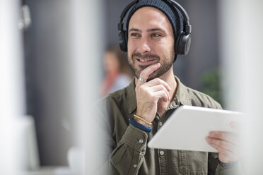 Portrait of smiling young man with headphones and tablet in office - ZEF15524