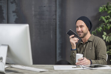 Smiling young man with cell phone at desk in office - ZEF15525