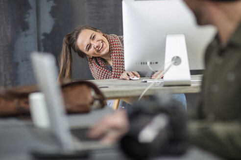 Glückliche junge Frau, die im Büro um den Computerbildschirm herumschaut - ZEF15533