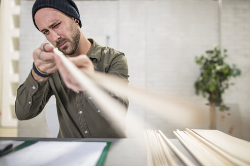 Junger Mann arbeitet mit Holz am Schreibtisch im Büro - ZEF15544