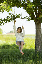 Smiling young woman sitting on swing - MAEF12618