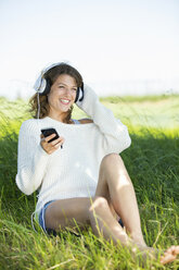 Lächelnde junge Frau mit Kopfhörern und Smartphone beim Musikhören - MAEF12623