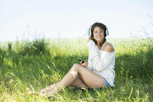 Lächelnde junge Frau mit Kopfhörern und Smartphone beim Musikhören - MAEF12624