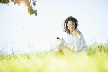 Lächelnde junge Frau mit Kopfhörern und Smartphone beim Musikhören - MAEF12625