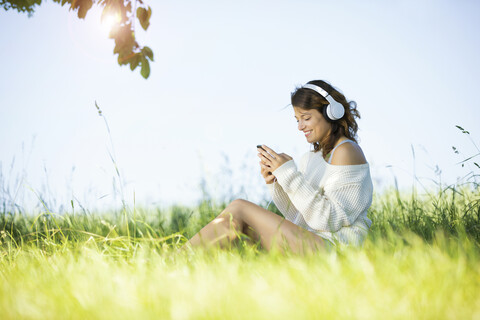 Lächelnde junge Frau mit Kopfhörern und Smartphone beim Musikhören, lizenzfreies Stockfoto