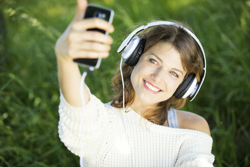 Lächelnde junge Frau mit Kopfhörern, die ein Selfie macht - MAEF12628