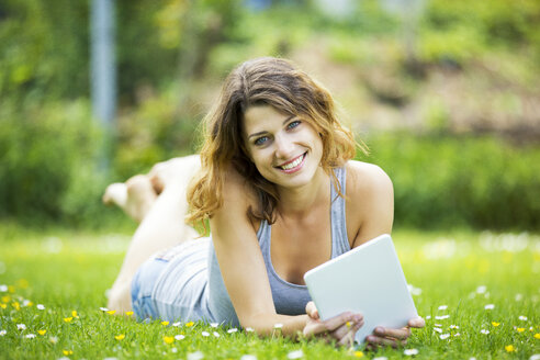 Lächelnde junge Frau liegt auf einer Wiese und benutzt ein Tablet - MAEF12632