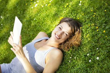 Young woman lying on meadow, using tablet - MAEF12634