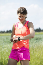 Lächelnde junge Frau, die eine Pause vom Sport macht und auf ihre Smartwatch schaut - MAEF12643