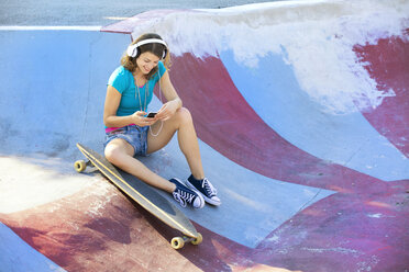 Female longboarder with earphones using smartphone - MAEF12651