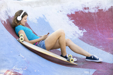 Female longboarder with earphones lying in halfpipe - MAEF12652