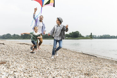 Happy father with two sons flying kite at the riverside - UUF13923