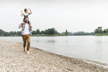 Glücklicher Vater trägt seinen Sohn auf den Schultern am Flussufer - UUF13924