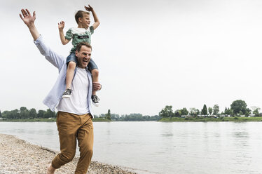 Glücklicher Vater trägt seinen Sohn auf den Schultern am Flussufer - UUF13925