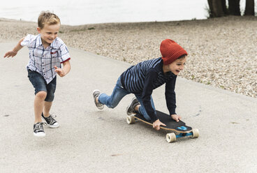 Glücklicher Junge läuft neben seinem Bruder auf dem Skateboard - UUF13937