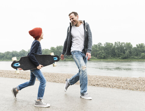 Happy father and son with skateboard at the riverside stock photo