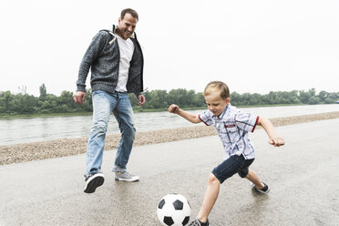 Glücklicher Vater und Sohn beim Fußballspielen am Flussufer - UUF13946