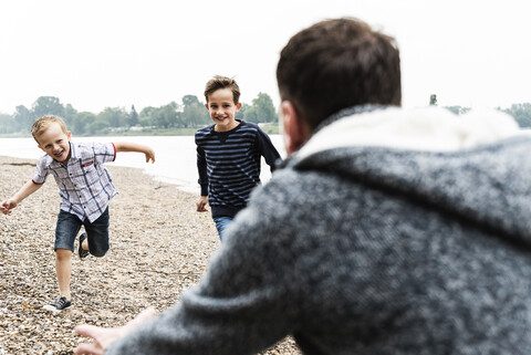 Glückliche Jungen, die ihrem Vater am Flussufer entgegenlaufen, lizenzfreies Stockfoto