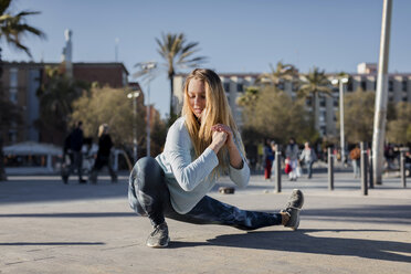 Spain, Barcelona, woman stretching leg on beach promenade - MAUF01419