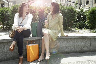 Zwei Frauen mit Einkaufstaschen sitzen an der Wand und unterhalten sich, Mailand, Italien - CUF21237
