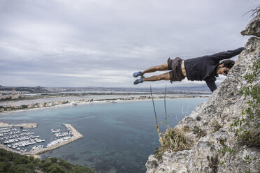 Male rock climber balancing horizontally mid air on coastal rock, Cagliari, Italy - CUF21249