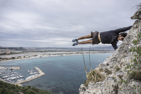 Männlicher Kletterer balanciert waagerecht in der Luft auf einem Küstenfelsen, Cagliari, Italien - CUF21249