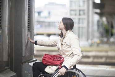 Young woman using wheelchair pressing control for city elevator - CUF21284