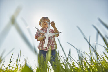 Low angle view of boy standing in grass checking toy airplane tail - CUF21302
