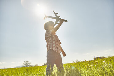 Boy in sunlit field with blue sky playing with toy airplane - CUF21303