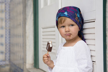 Portrait of female toddler leaning against shutters eating ice lolly, Beja, Portugal - CUF21306
