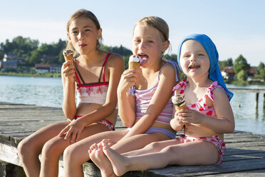 Zwei Schwestern und ein weibliches Kleinkind essen auf einem Steg Eiswaffeln, Seeoner See, Bayern, Deutschland - CUF21309