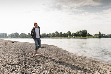Älterer Mann mit roter Mütze beim Spaziergang am Rheinufer - UUF13963