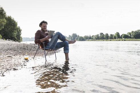 Mature man using tablet at Rhine riverbank - UUF13971