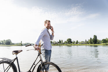 Älterer Mann mit Fahrrad und Smartphone am Rheinufer - UUF13974