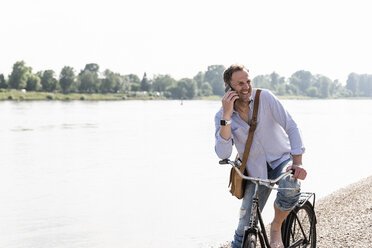 Älterer Mann mit Fahrrad und Smartphone am Rheinufer - UUF13976