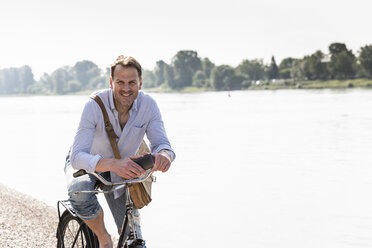 Mature man with bike and smartphone at Rhine riverbank - UUF13977