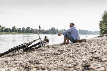 Älterer Mann mit Fahrrad am Rheinufer sitzend - UUF13980