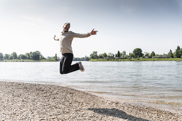 Mature man jumping in the air at Rhine riverbank - UUF13994